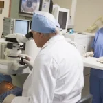 An ophthalmologist examines a patient’s eyes while their colleague assists on a medical computer.